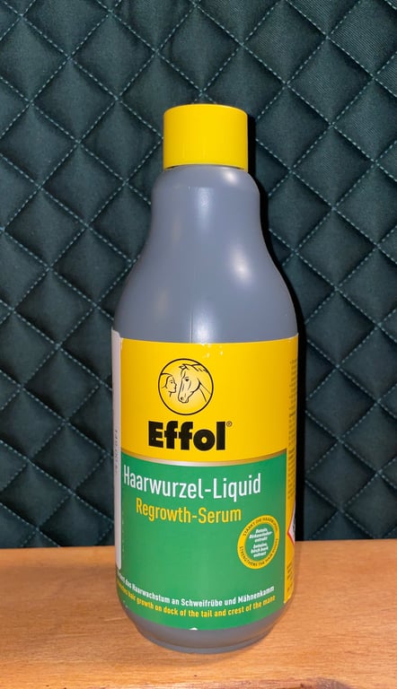 Flaske med Effol Haarwurzel-Liquid Regrowth-Serum til hårvækst, placeret på en træs overflade med mørk quiltet baggrund.