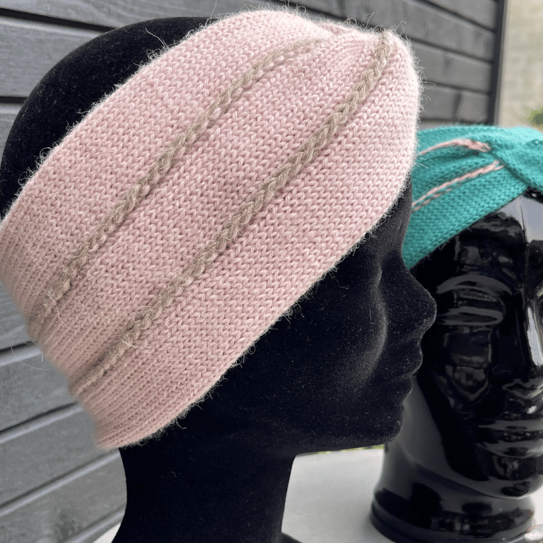 To sort mannequinhoved med strik pandebånd, det nærmeste i lyserød med beige striber, og det bageste i turkis med lyserøde striber.