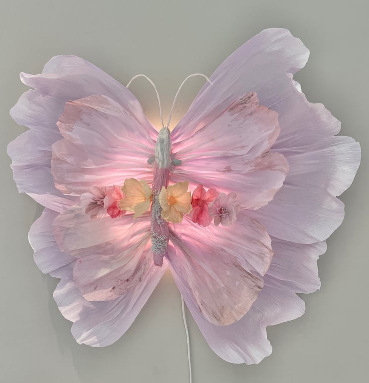 En dekorativ sommerfugl lavet af lyserøde blomsterblade og kunstige blomster med en blød lysende effekt.