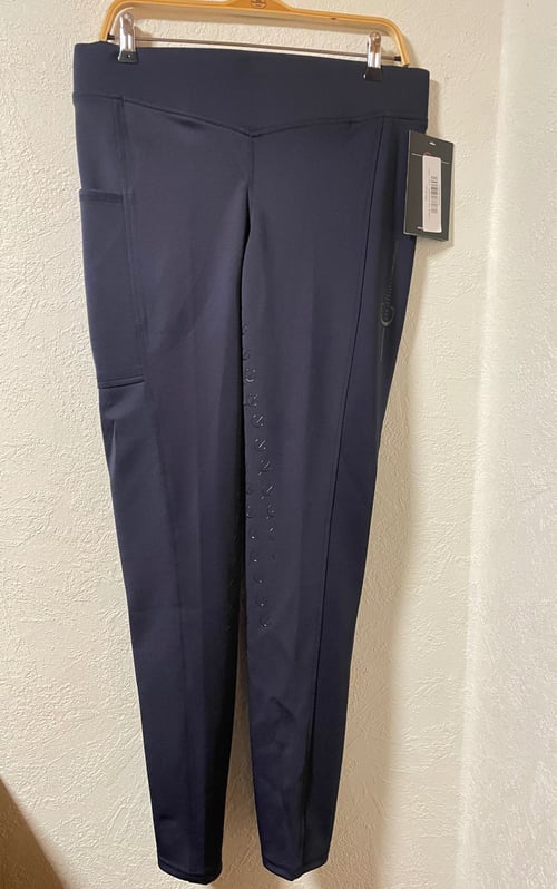 Mørkeblå leggings med sidelommer hængende på en gul bøjle mod en hvid væg. (1)