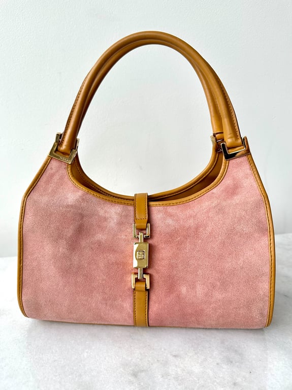 Rosa ruskinds håndtaske med brune læderhåndtag og guldfarvet spænde foran.