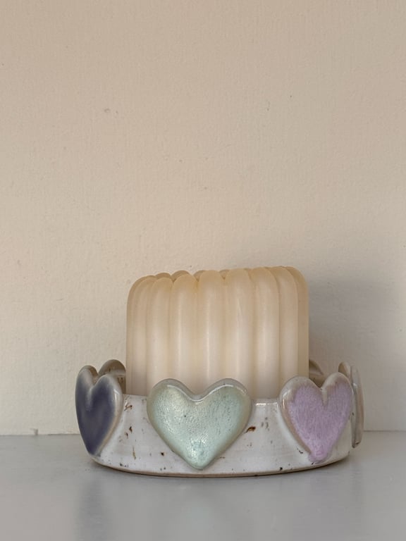 Et lys i et hvidt lysestage med pastelfarvede hjerter i blå, grøn og lilla.