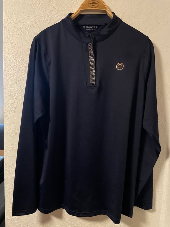 Langærmet, mørkeblå sportsbluse med kort lynlås og lille logo på brystet, hængende på en træbøjle mod en hvid væg.