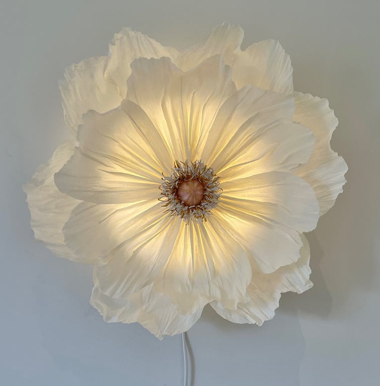 Stor dekorativ hvid blomst formet lampe tændt på væggen med bløde folderede kronblade.