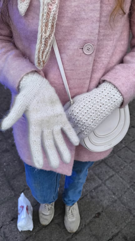 Person iført lyserød uldjakke, hvide strikkede handsker og lyse sneakers, der holder en lille hvid rund taske.