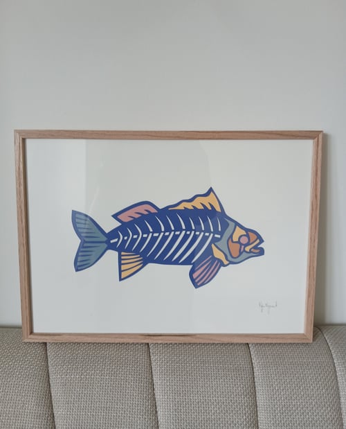 Tegning af en fisk med synlige, stiliserede fiskeben i blå, orange og pink toner, indrammet med en træramme og placeret på en beige sofa. (2)