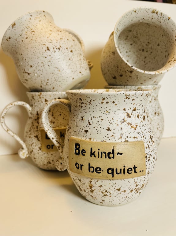 Flere keramikkrus med brunlige pletter, hvoraf et har teksten "Be kind or be quiet." skrevet på en label.
