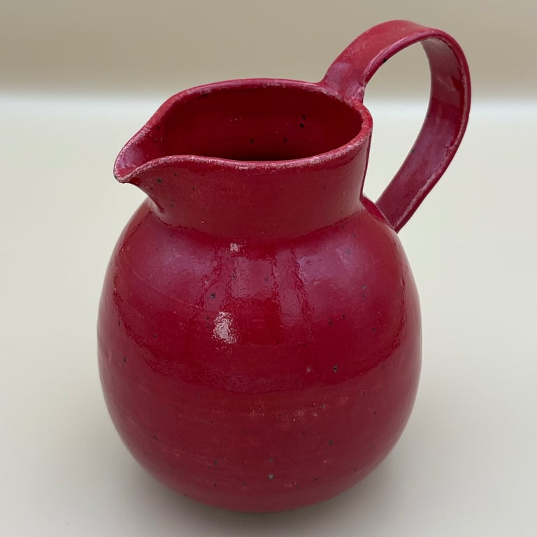 Rød keramisk kande med håndtag og lille tud på hvid baggrund.