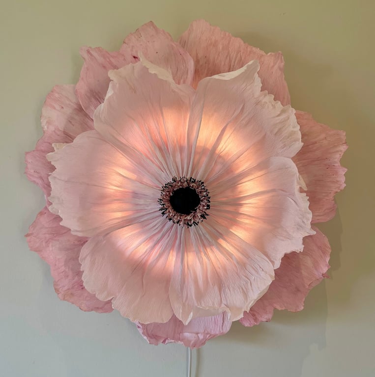 Stor, lysende pink blomst formet lampe hængende på væggen.