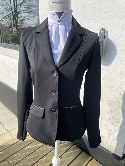 Sort ridejakke med tre knapper og hvid ridebluse på mannequin, fotograferet udendørs foran hvid væg. (2)