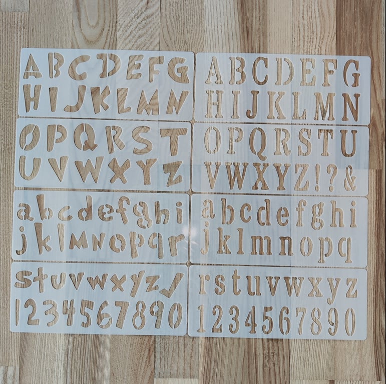 To sæt af bogstavskabeloner i forskellige typografier med både store og små bogstaver samt tal, lagt ud på et lyst trægulv.