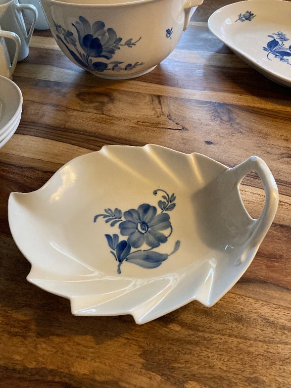 Hvidt porcelænsfad formet som et blad med blå blomsterdekor på, placeret på et træbord. (2)