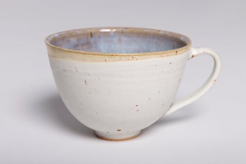 En hvid keramisk kop med en let buet form og en elegant håndtag, indvendigt med en blå-lilla glaze.