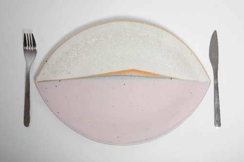 Oval tallerken med abstrakt farvet design i hvid og lyserød, placeret mellem en gaffel til venstre og en kniv til højre på hvid baggrund.