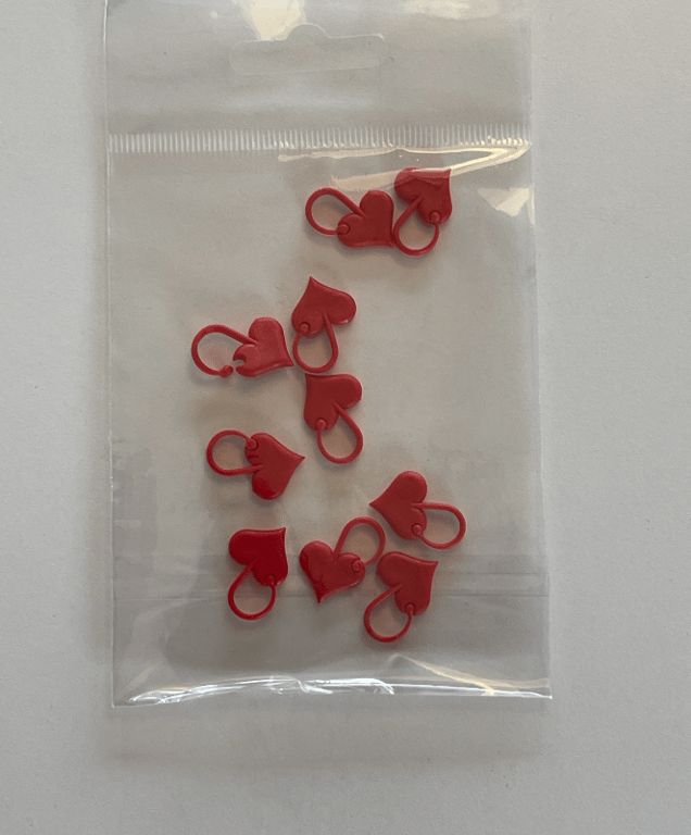 Plastpose med ti små røde hjerteformede markører eller clips på hvid baggrund.
