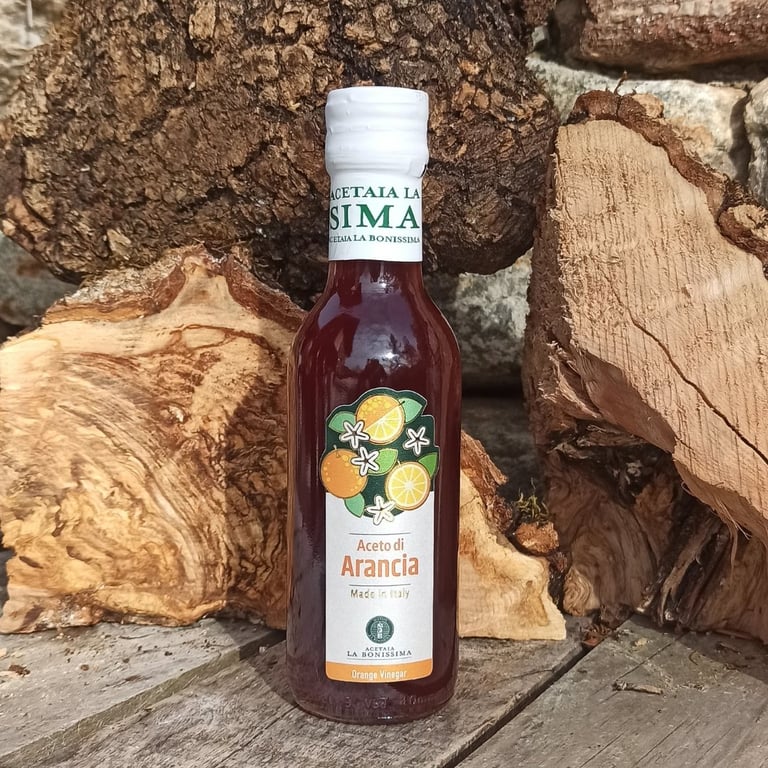 Flaske med italiensk appelsinedressing (Aceto di Arancia) placeret foran stablet træ.