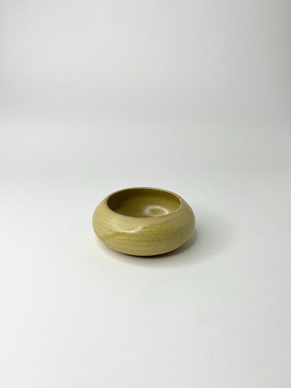 Grønlig, glaseret keramikskål med rund, lav form placeret på hvid baggrund.