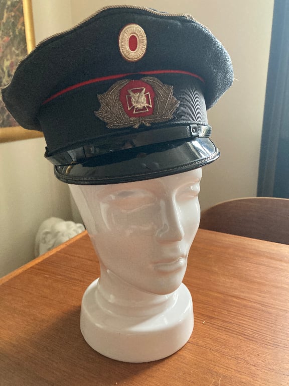 Mannequinhoved med sort og rød uniformskasket med emblem på et træbord.