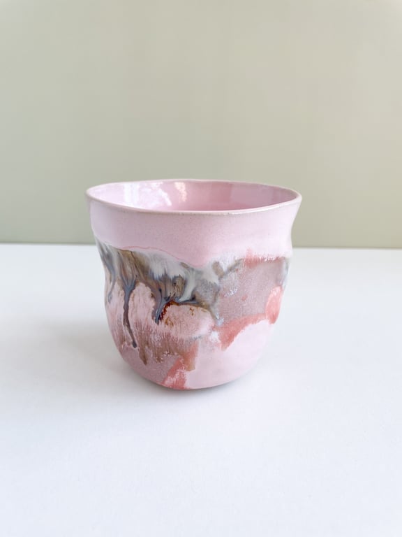 Lyserød keramikkop med abstrakte farvepletter i brun, hvid og grå, placeret på hvid overflade.