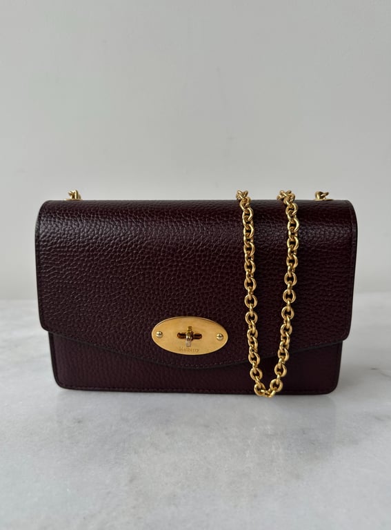 Mørk bordeauxfarvet lædertaske med gyldent kæderemme og oval guldspænde.
