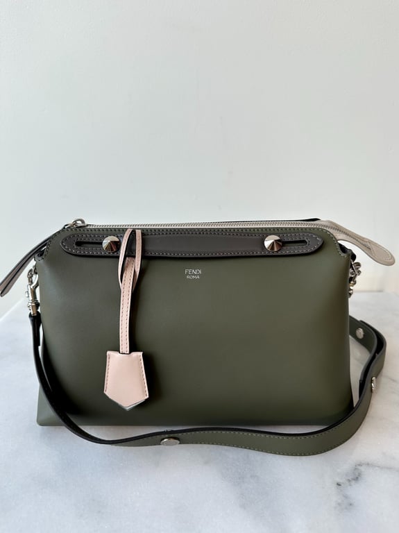 Grøn Fendi skuldertaske med lyserødt lædervedhæng og sort justerbar rem, placeret på hvid overflade mod en hvid væg.