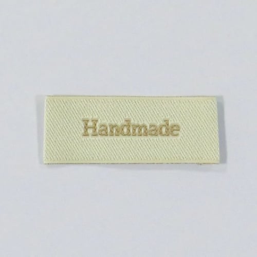 Hvidt stofmærke med tekst "Handmade" i beige. (1)