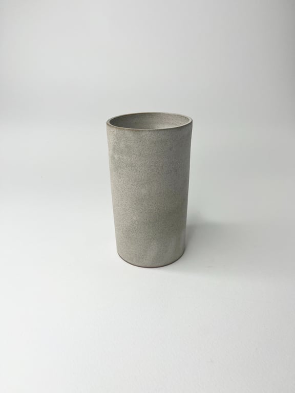 Grå, cylindrisk kop i keramik på hvid baggrund.
