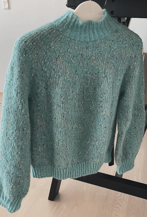 Lyseblå, strikket sweater med pufærmer og høj hals hænger på en bøjle. (3)