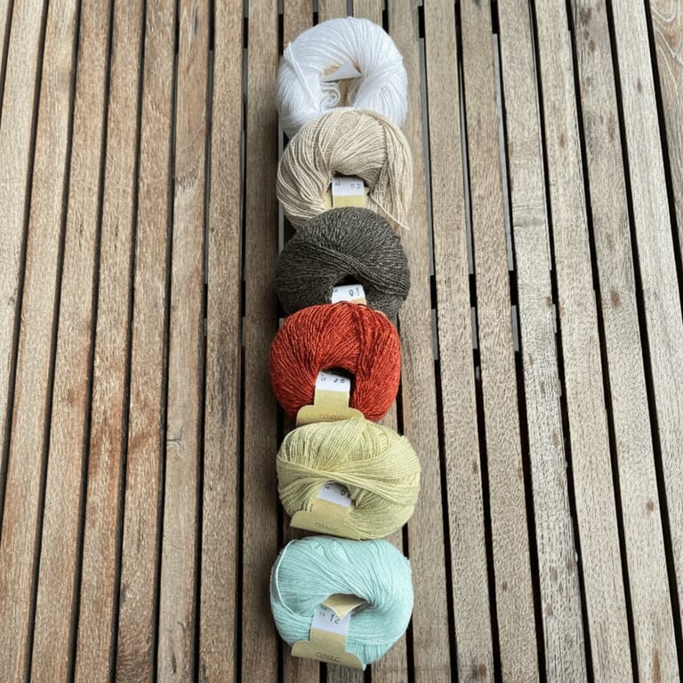 Seks nøgle garn i forskellige farver arrangeret i en lodret række på et brunt træbord.