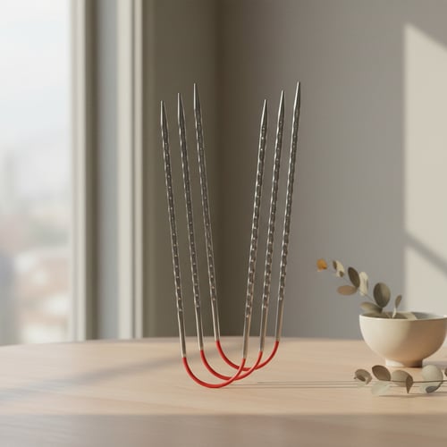 Seks lange metalprikker krummet i bunden og samlet i en U-form, stående på et lyst træbord ved siden af en hvid skål med tørrede blade. (3)