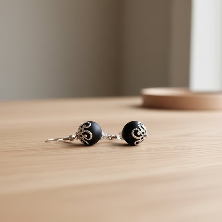 To sorte perleøreringe med dekorative sølvbeslag lagt på en lys træbordplade.
