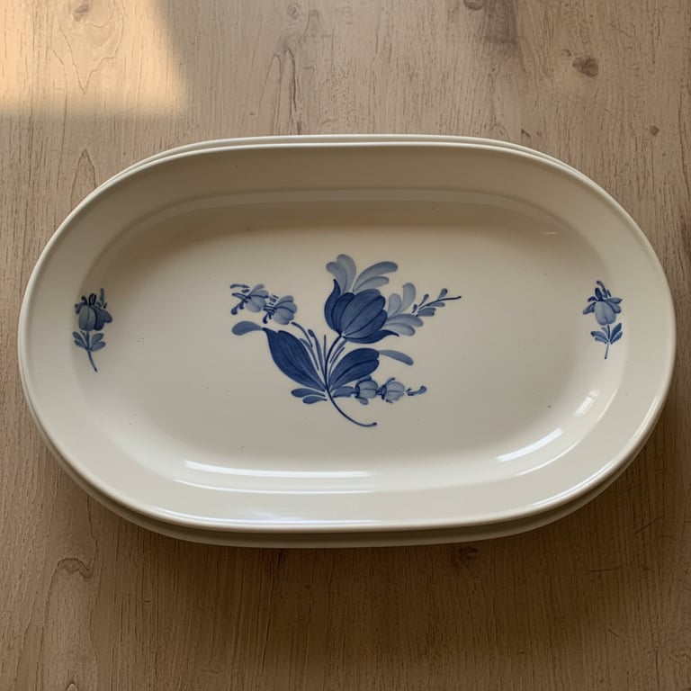 Oval hvid porcelænsfad med blå blomsterdekoration, placeret på et lyst træbord.