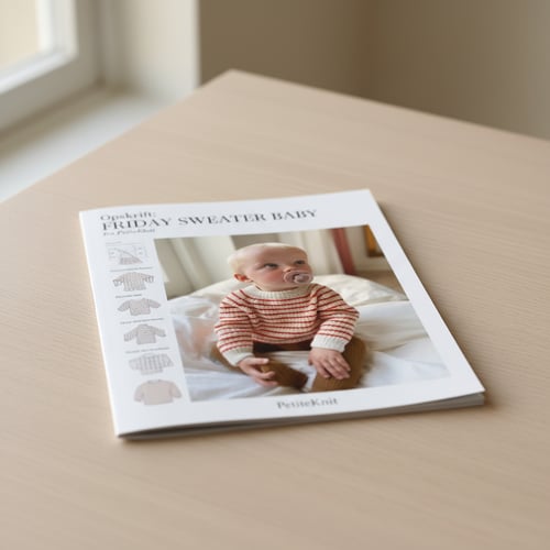 Strikkeopskrift hæfte til babytrøje med billede af baby i stribet sweater på forsiden, lagt på lyst træbord. (3)