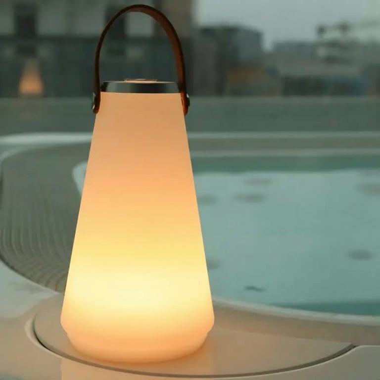 Lysende, konisk havelampe med brunt bærehåndtag placeret ved kanten af et udendørs bassin i skumringen.